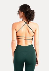 Grön sport-bh med tunna remmar och korsryggsdesign. Texturerat tyg med slät yta och justerbart spänne bak.