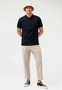 Polo blu navy a maniche corte, pantaloni beige su misura e sneakers nere. Il modello indossa un cappello a tesa larga beige chiaro. Design semplice.