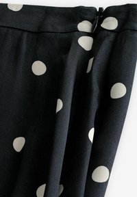 Tissu noir à gros pois blancs et fermeture éclair noire partiellement visible sur le bord supérieur.