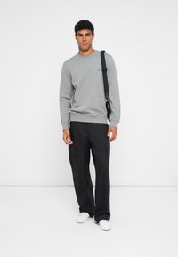 Felpa grigia con scollo rotondo, polsini e orlo a coste. Pantaloni cargo neri con tasche multiple. Sneakers bianche. Modello in piedi su uno sfondo neutro.
