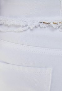 Tela de mezclilla blanca con bordes deshilachados y un bolsillo. La textura es suave, con costuras visibles y un ligero brillo.