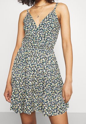 Robe d'été florale avec un corsage ajusté, un décolleté en V et une taille smockée. Elle présente un fond bleu marine avec de petites fleurs jaunes et blanches.