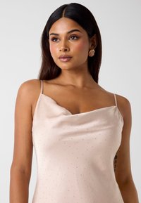 Satynowa sukienka z kołnierzem typu cowl w jasnoróżowym kolorze z cienkimi ramiączkami, ozdobiona małymi, subtelnymi koralikami, tworzącymi fakturowany i elegancki wygląd.