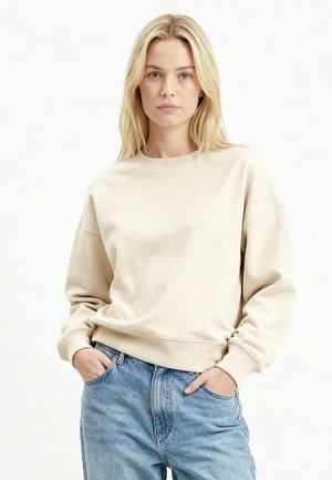 Beige sweater met ronde hals en een losse pasvorm, voorzien van geribbelde manchetten en zoom. Gecombineerd met lichtblauwe, hoog uitgesneden jeans. Eenvoudig ontwerp, casual uitstraling.