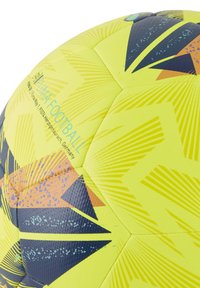 Žuta nogometna lopta s geometrijskim uzorcima u mornarsko plavoj i narančastoj boji. Teksturirana površina, heksagonalne ploče i vidljivo brendiranje.