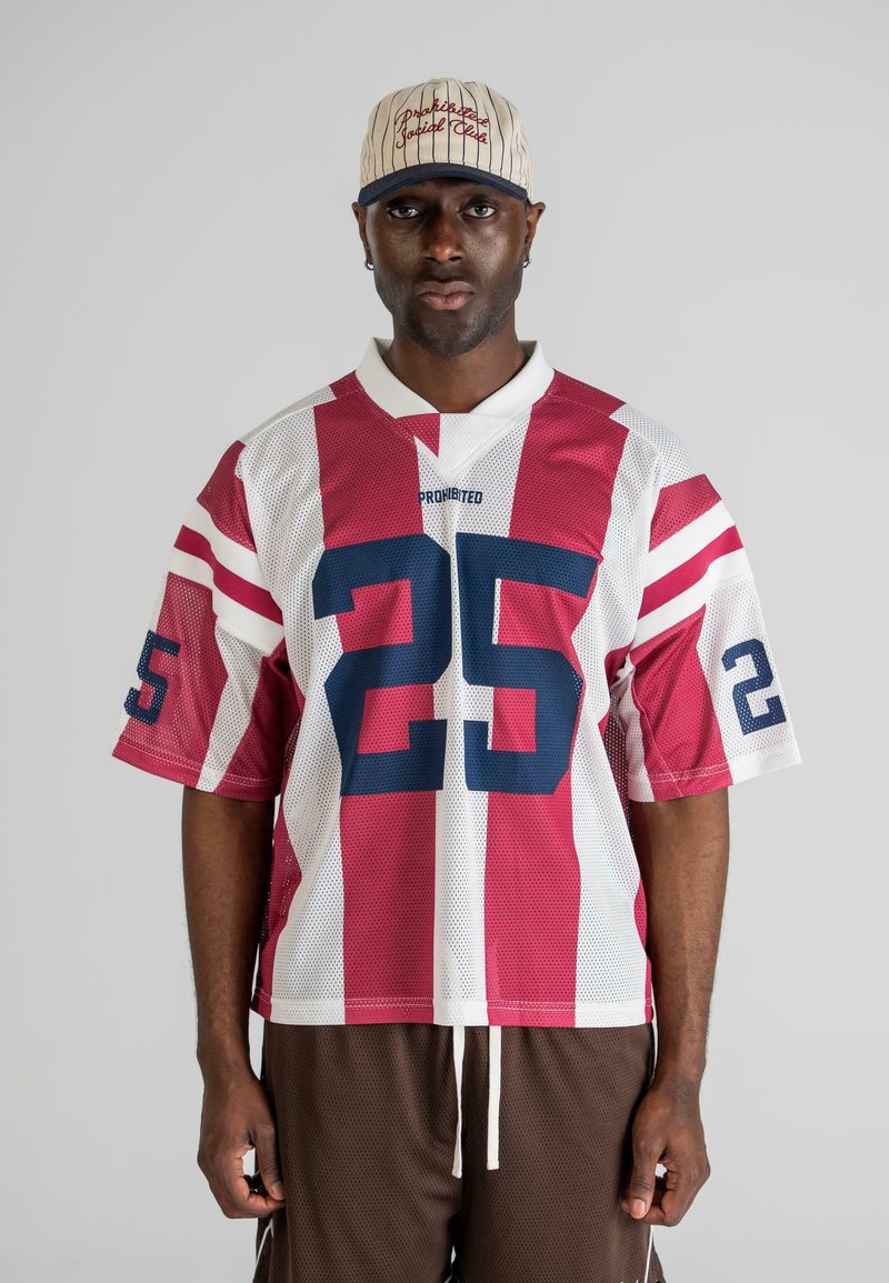Red and white striped mesh jersey with number 25 in navy, worn with brown shorts. Accompanied by a cream baseball cap with red text.