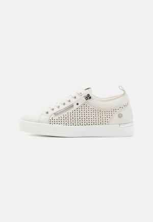 Zapatilla de color beige claro con diseño perforado en el lateral, suela blanca, parte frontal con cordones y acento decorativo de cremallera. Material suave con acabado texturizado.