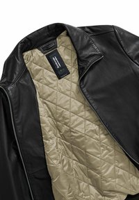 Giubbotto in pelle nera con fodera quilted beige. Presenta un colletto alto e una zip in metallo. Etichetta interna visibile vicino al colletto.