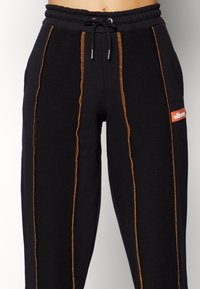 Zwarte sweatpants met oranje verticale naden, een trekkoord in de taille en een klein oranje logo op de rechterdij.