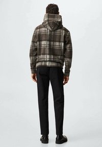 Sudadera con capucha de cuadros en marrón oscuro y gris con una capucha grande, hecha de tela suave. Combinada con pantalones negros y botines negros hasta el tobillo.