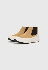 Botas de tobillo de ante marrón con lados elásticos negros, suela de goma blanca y suela exterior texturizada negra para mayor agarre.
