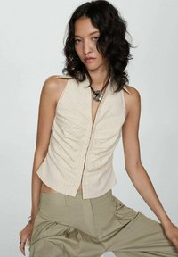 Beige přiléhavý top s halter krkem, s vertikálními pruhy a nařaseným předním designem; doplněný uvolněnými, světle khaki kalhotami.