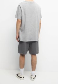 T-shirt en coton gris à manches courtes, assorti à un short gris. Les accessoires comprennent des chaussettes blanches et des baskets crème avec des accents noirs.