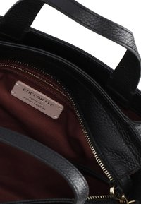 Borsa a tracolla in pelle nera con superficie testurizzata. L'interno presenta una fodera di un rosso scuro e un'etichetta con la scritta "Coccinelle, Pelle Italiana Autentica."