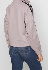 Lavendel sweatshirt med hög krage, svarta sidostråkar och ribbade ärmslut; kombinerad med mörkblå jeans med bakfickor.