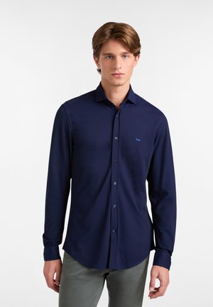 Camicia a maniche lunghe di colore blu scuro con colletto button-down, dotata di un piccolo logo azzurro sul petto e bottoni coordinati. Texture del tessuto liscia.