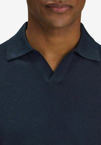 Navy blue knitted polo shirt with a v-neck, ribbed texture, and structured collar. Close-up view focusing on neckline and upper fabric details.
