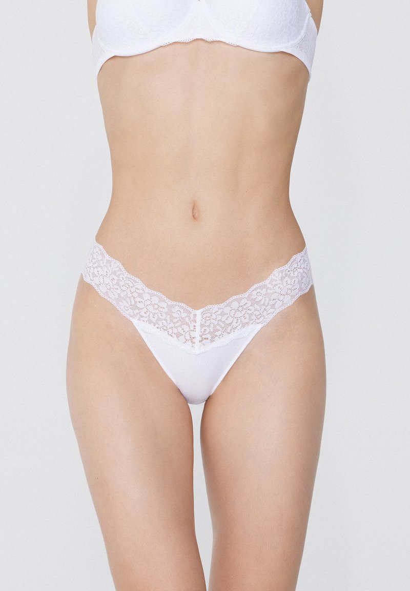 Weiße Spitzen-Tanga-Unterwäsche mit weichem Stofffinish. Der Spitzenbund zeigt Blumenmuster. Minimalistisches Design in V-Form.