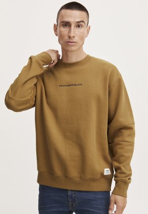 Bruine sweater met geribbelde ronde hals, oversized pasvorm, en zwarte tekst "streef naar iets stevigs" gecentreerd op de borst. Katoenen materiaal.