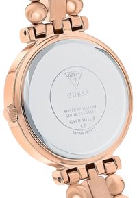 Złoto-tonowana stal nierdzewna z gładką srebrną powierzchnią, z widocznym napisem "Guess", numerem modelu i informacjami o odporności na wodę.
