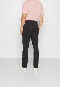 Svarta byxor med rakt ben, tillverkade av ett slätt tyg. Har två bakfickor och är kombinerade med vita sneakers.