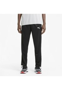 Sorte træningsbukser med et tapered fit, elastisk talje og hvid Puma-logo på venstre lår. Bæres med sorte og hvide sneakers.