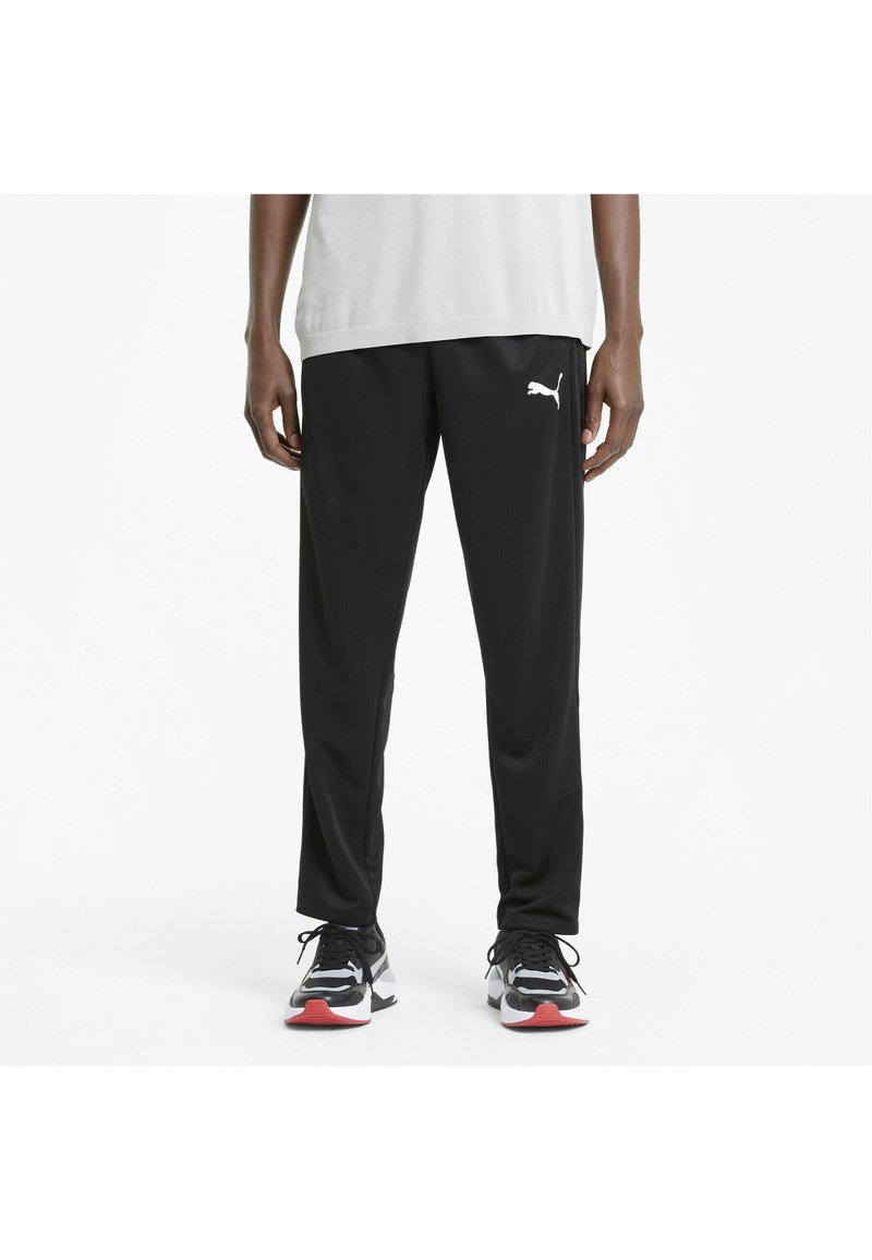 Sorte træningsbukser med et tapered fit, elastisk talje og hvid Puma-logo på venstre lår. Bæres med sorte og hvide sneakers.