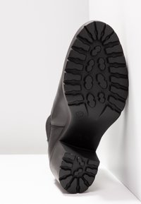 Semelle de chaussure noire avec motif de empreintes profondes, en caoutchouc. Présente un bord arrondi et une étiquette indiquant la taille 37. Surface texturée pour l'adhérence.