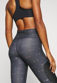 Leggings neri con motivo di testo "AIR" multicolore. Presentano un alto fodero in vita, un pannello in rete sul lato e una tasca con zip sul retro.