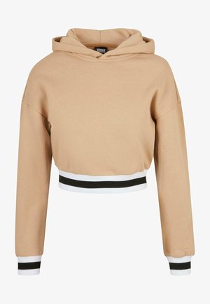 Sweat à capuche court beige avec manches longues, poignets et taille côtelés à rayures noires et blanches, et une capuche à l'avant.