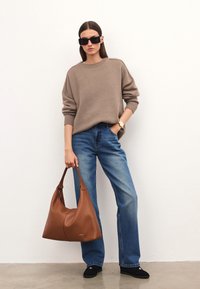 Brązowy sweter z dzianiny, niebieskie jeansy z wysokim stanem i duża brązowa skórzana torba na ramię. Czarne okulary przeciwsłoneczne i zegarek dopełniają strój.