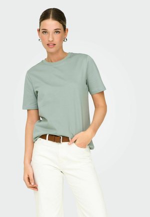 Light green cotton t-shirt with short sleeves and a crew neckline, paired with white pants and a brown belt. Simple, casual design.