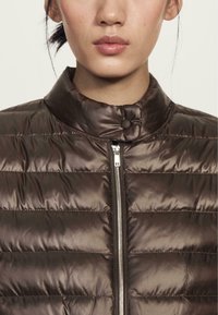 Brown padded jacket with a high collar, featuring horizontal quilted sections, a zipper front, and a front snap button detail.