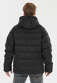 Veste en duvet noire avec capuche, design matelassé et poignets élastiques. Texture lisse avec une fermeture éclair en bas des côtés.