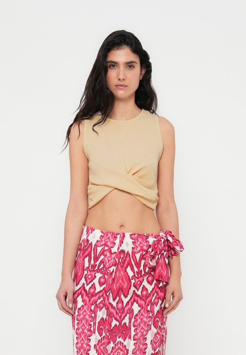Μπεζ ριμπ τοπ cropped με σχέδιο στρίφωμα στο μπροστινό μέρος, συνδυασμένο με ροζ και λευκή φούστα με σχέδιο και λεπτομέρεια ζώνης στο μέση.