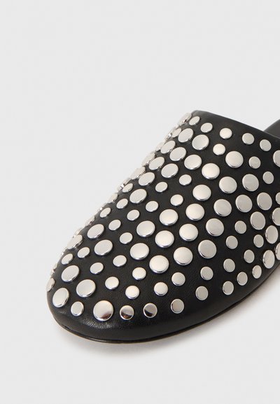 Chaussure noire en cuir à enfiler ornée de clous circulaires métalliques argentés de différentes tailles, répartis uniformément sur la surface supérieure.