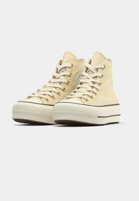 Υψηλές αθλητικές κάλτσες από φωτεινό κίτρινο ύφασμα με τονι κό σχέδιο, κρεμ κορδόνια, στρογγυλή μύτη, καουτσούκ σόλα και μαύρη λωρίδα λεπτομέρειας στη μέση.