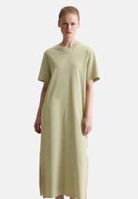 Lichtgroene katoenen T-shirt jurk met korte mouwen, ronde halslijn en zijsplitten voor gemakkelijk bewegen, met een ontspannen pasvorm.