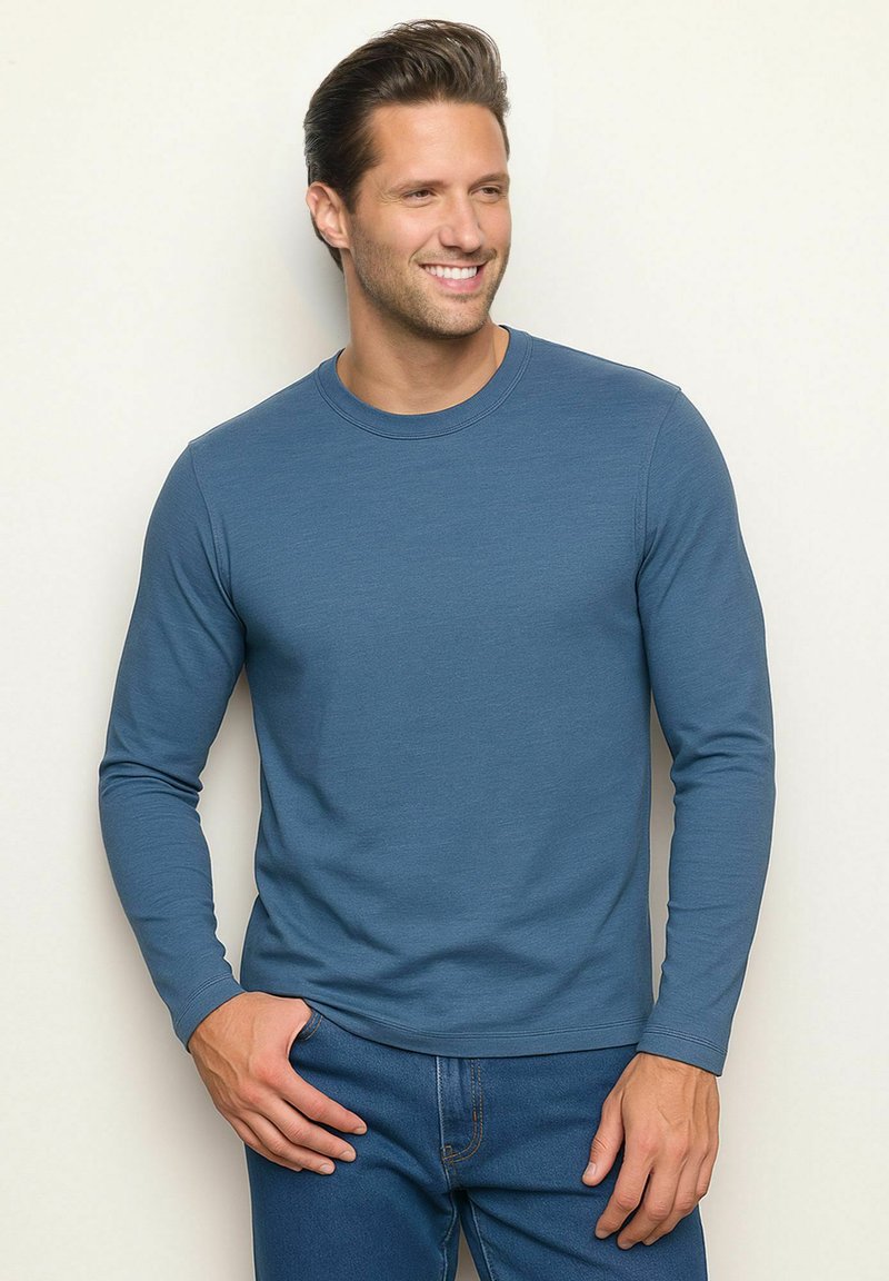 Maglietta a maniche lunghe con collo rotondo di colore blu intenso, realizzata in un tessuto morbido, abbinata a jeans blu scuro, con una vestibilità relaxed.