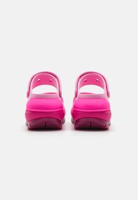 Crocs roz cu un finisaj lucios neted, având două curele în spate și orificii de ventilație pe laturi pentru o respirabilitate mai bună.
