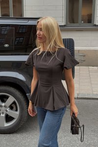 Blonde Frau trägt ein schwarzes Peplum-Top und blaue Jeans, hält eine schwarze Handtasche und steht neben einem schwarzen Land Rover auf einer Straßen in der Stadt.