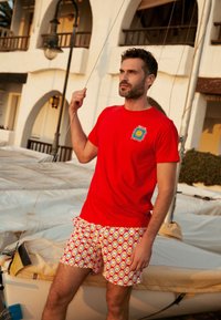 Rode katoenen T-shirt met een kleurrijke afbeelding en een korte broek met een bloemenpatroon in gele, oranje en blauwe tinten.