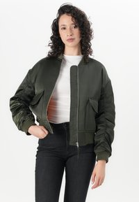 Oliven grønn bomberjakke med satinfinish, med glidelås, to frontlommer og ribbede mansjetter. Jevn tekstur og kort design.