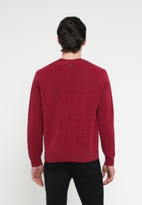 Punane kootud kampsun, millel on pikad varrukad ja ümar kaelus, mis on kaunistatud tekstuurse mustriga ning soonikkoes mansettide ja alläärega.