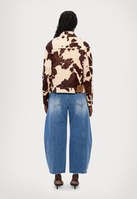 Brun och krämfärgad ko-mönstrad jacka med en kort design, i kombination med vida blå jeans i denim med en urtvättad look och rå fåll.