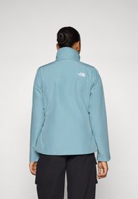 Giacca impermeabile azzurro chiaro con colletto alto e maniche lunghe. Caratterizzata da un piccolo logo bianco sul retro e tessuto liscio e morbido.