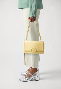 Yellow leather handbag with a structured design, featuring a rectangular shape, flat front, and a prominent buckle detail. Smooth texture.