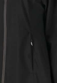Svart vattentät jacka med en slät yta, sidoficka med dragkedja och kontrastsömmar längs dragkedjan.