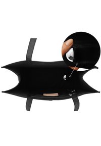 Interno di una borsa tote nera con tasca laterale che contiene un AirTag bianco, mostrato in un primo piano di una mano che inserisce l'AirTag nella tasca.