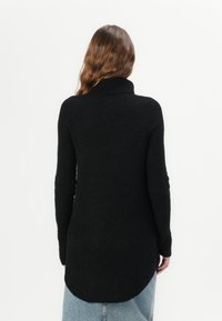 Maglione nero a trama con collo alto, maniche lunghe e orlo curvo, indossato sopra jeans blu, che mette in evidenza un design a costine.